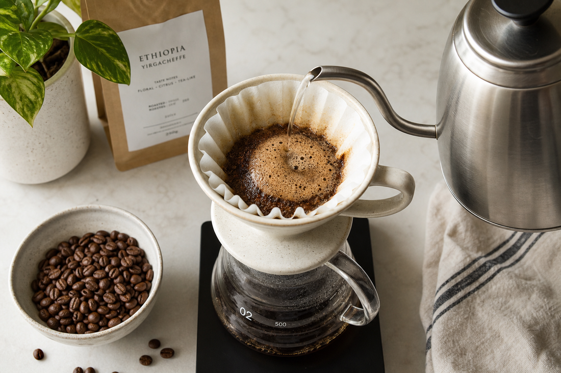 Ceramic pour over dripper brewing coffee beside whole beans and a gooseneck kettle on a countertop