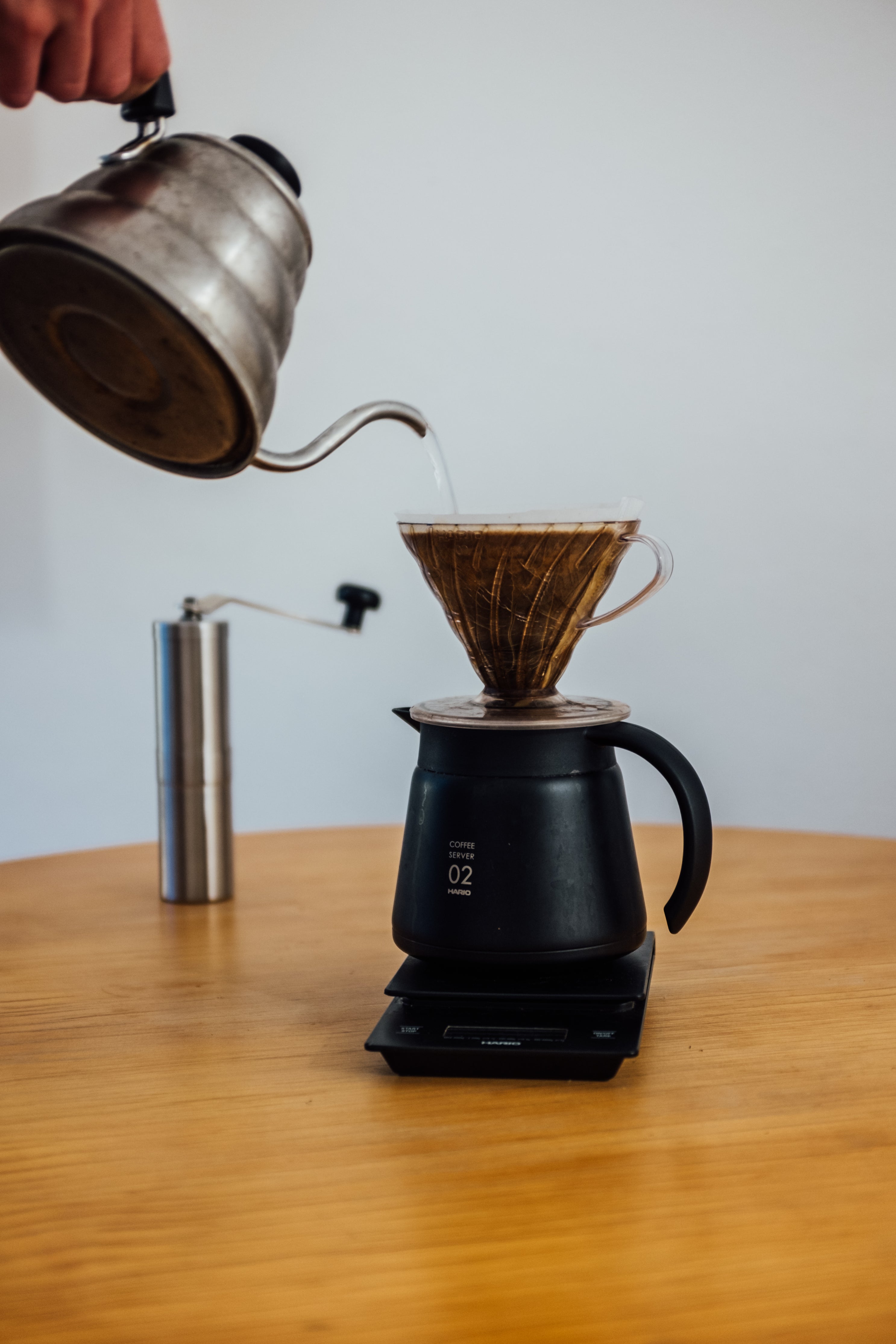 wooden table with a scale holding a coffee pot with hand pouring from above