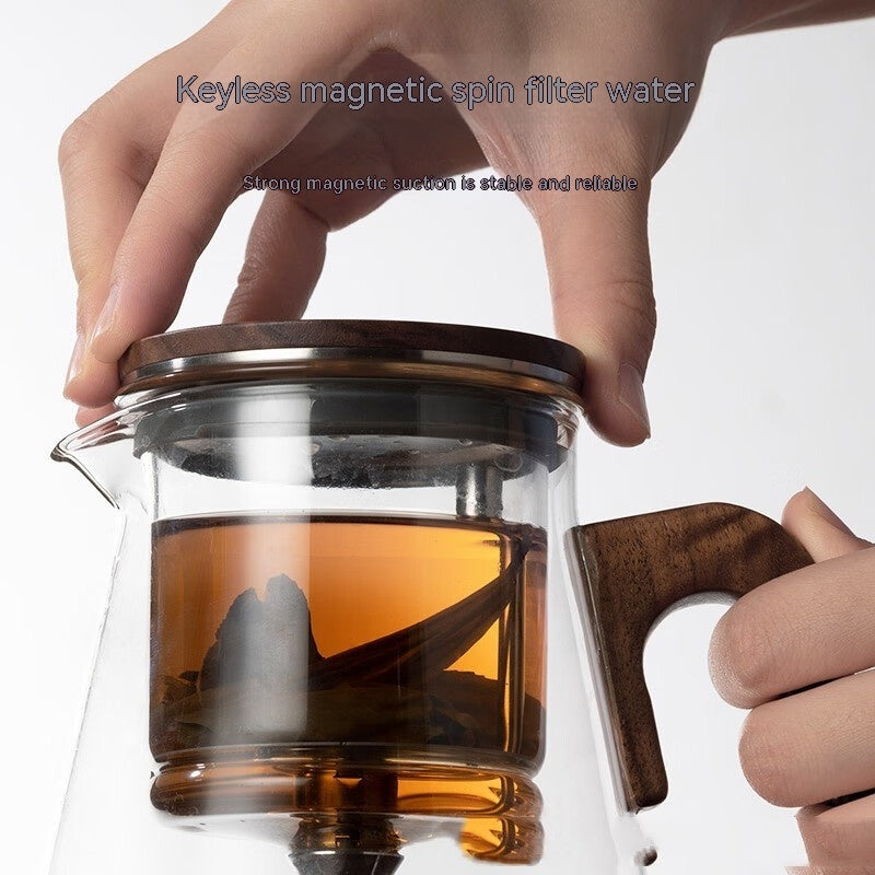 One-Click Filtering Glass Teapot with a walnut wood handle and glass liner. Features a keyless magnetic spin filter for effortless tea brewing.