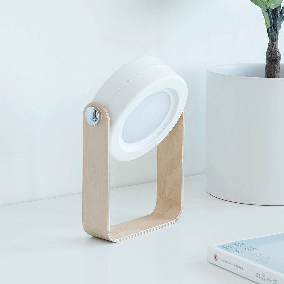 Foldable LED night light in a compact position on a wooden stand. USB rechargeable lamp with touch dimmable brightness for modern decor.