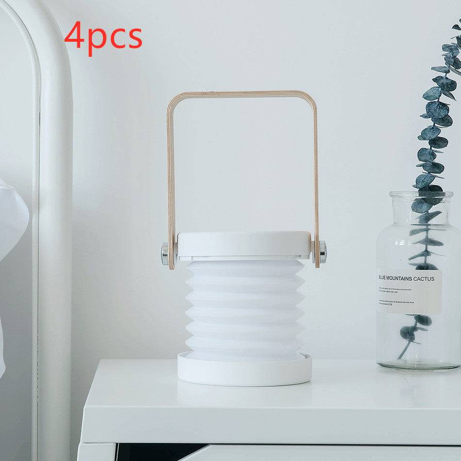 Set of four white foldable LED night lights placed on a bedside table. USB rechargeable lantern with touch dimmable brightness control.
