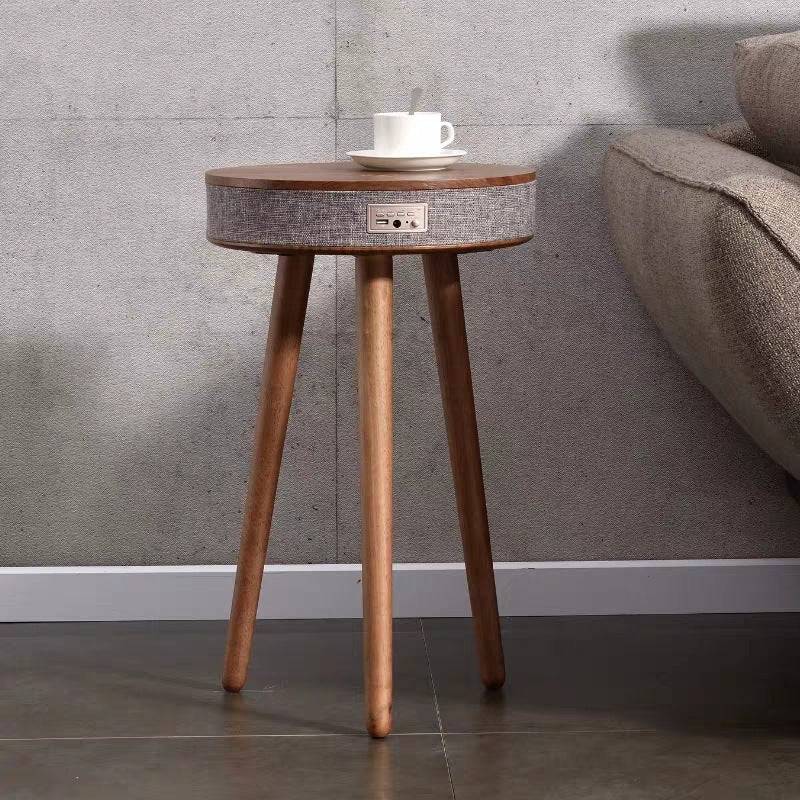 Minimalist Bluetooth speaker coffee table with wireless charging, placed beside a sofa with a cup on top. Blends functionality with modern aesthetics.