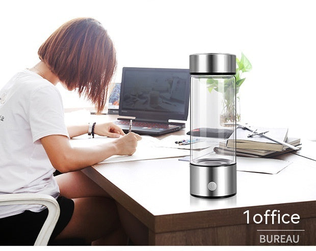 A woman working at a desk with a silver hydrogen water bottle nearby. Portable and rechargeable, ideal for office use and healthy hydration.