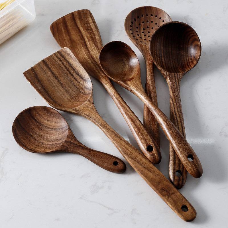 Teak wood kitchen set from Thailand featuring spoons, ladles, and turners in a glass measuring cup. Durable and eco-friendly tableware for cooking.