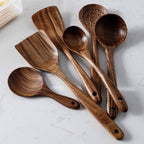 Teak wood kitchen set from Thailand featuring spoons, ladles, and turners in a glass measuring cup. Durable and eco-friendly tableware for cooking.