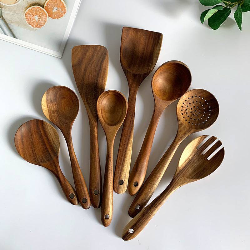 Teak wood kitchen set from Thailand featuring spoons, ladles, and turners in a glass measuring cup. Durable and eco-friendly tableware for cooking.
