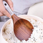 Teak lacquer rice paddle with ergonomic handle scooping white rice with black sesame seeds. Durable, eco-friendly Japanese-style kitchen utensil.