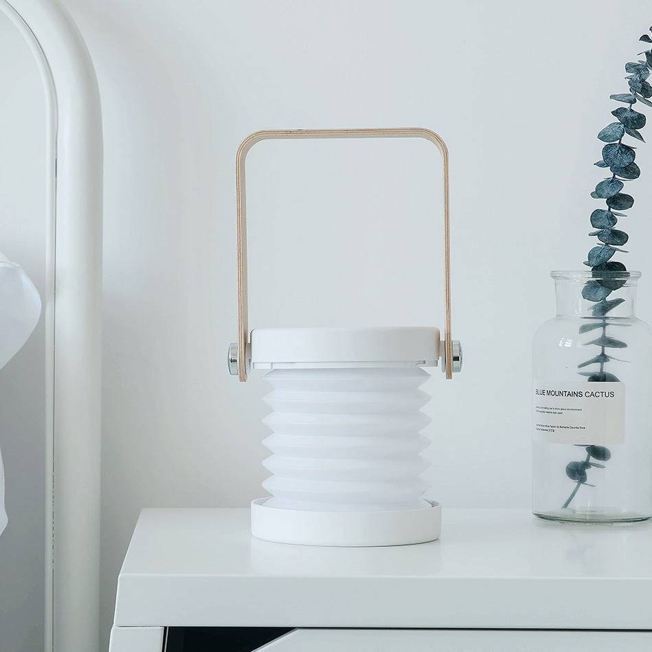 Single white foldable LED night light placed on a bedside table. USB rechargeable lantern with touch dimmable brightness for home decor.