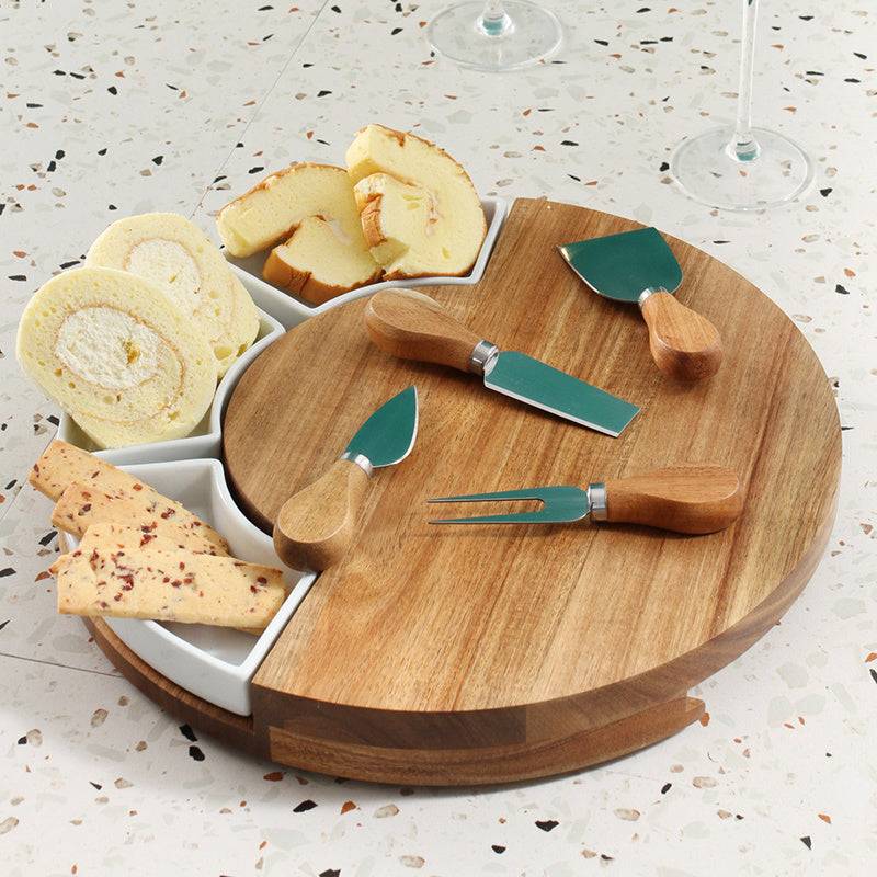Wooden cheese board with cutlery and assorted cheeses on a speckled surface