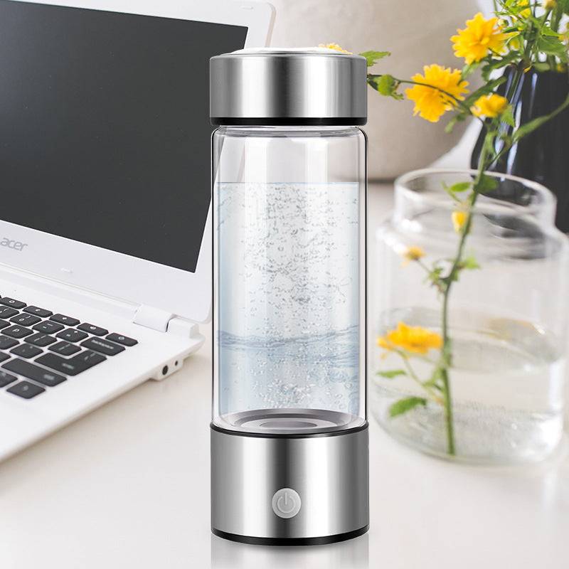 Silver hydrogen water bottle placed on a desk near a laptop and flowers. Electric and rechargeable, perfect for daily hydration with antioxidant benefits.