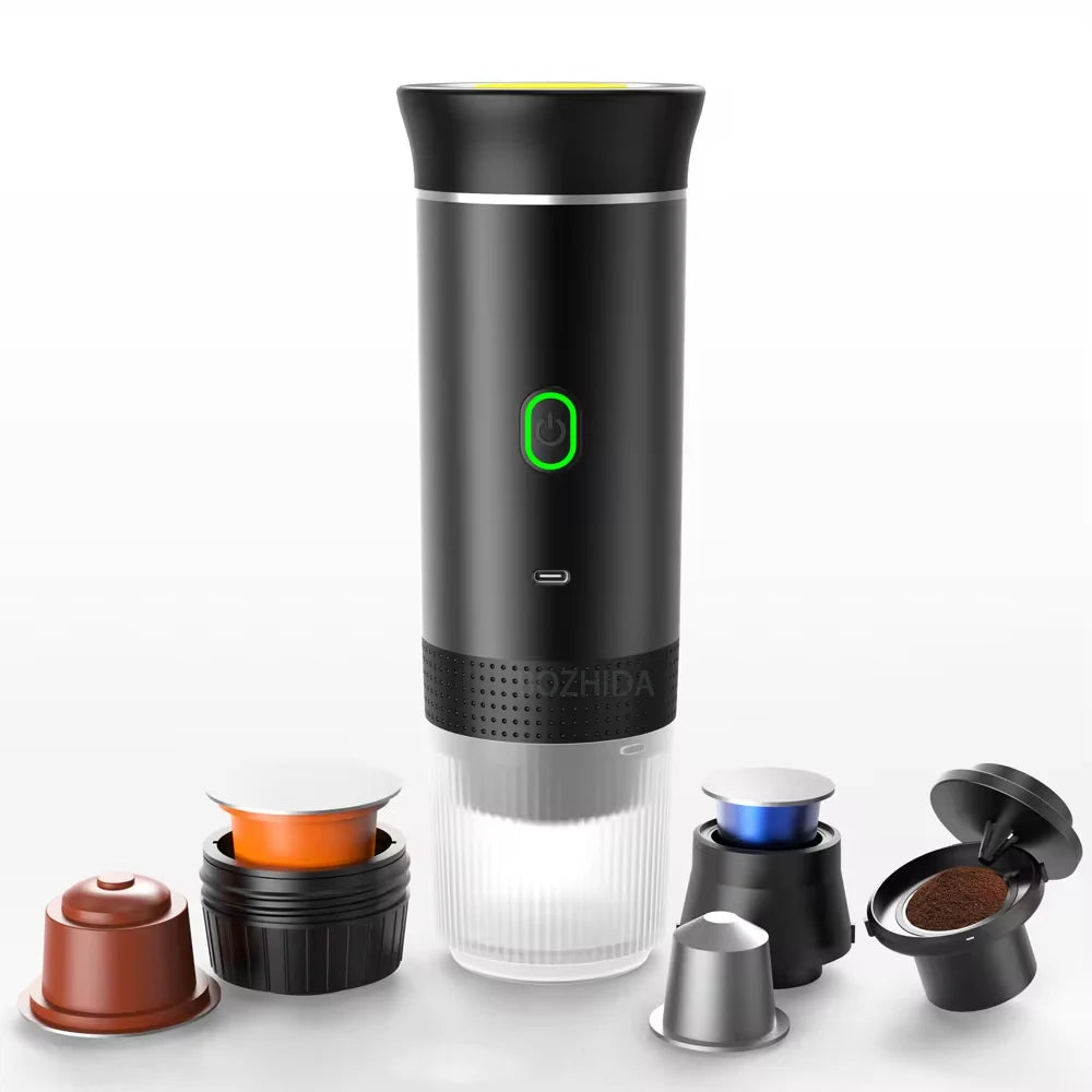 Portable black espresso machine with a transparent base, power button with a green ring, and various coffee capsules nearby.