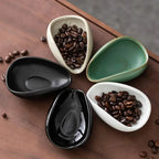 Set of four ceramic coffee beans dosing cup trays in black, white, green, and speckled beige. Each pottery espresso bean scoop features a tapered spout and curved edges for precise pouring.