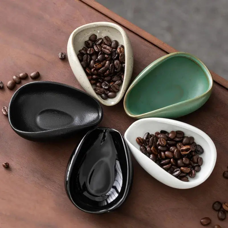 Set of four ceramic coffee beans dosing cup trays in black, white, green, and speckled beige. Each pottery espresso bean scoop features a tapered spout and curved edges for precise pouring.