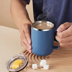 Person holding a blue mug with steaming coffee on a wooden surface