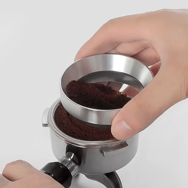 Hand using a silver coffee grinder to grind coffee beans on a white background
