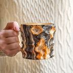 Hand holding a marbled ceramic mug against a neutral background
