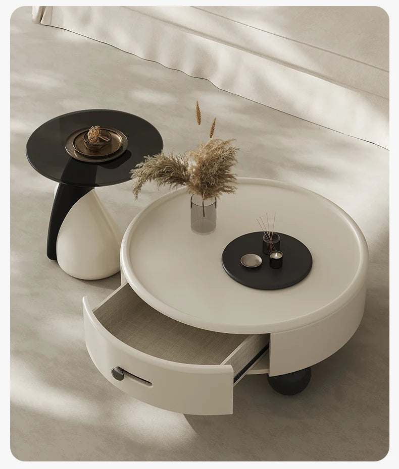 Round white coffee table with a drawer, black side table, and decorative items on a neutral background