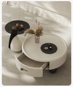 Round white coffee table with a drawer, black side table, and decorative items on a neutral background