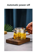 100°C Cup Heater Mug Warmer with automatic power-off, shown warming tea in a glass teapot on a wooden heating pad, ideal for hot beverages.