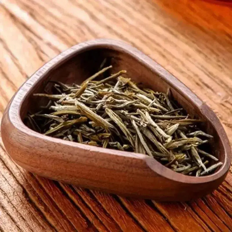 Wooden bowl filled with green tea leaves on a wooden surface