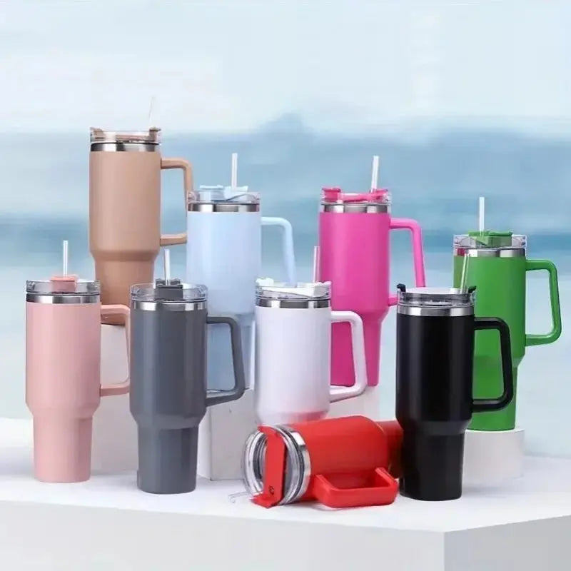 Collection of colorful insulated travel mugs with handles and straws on a blurred outdoor background.