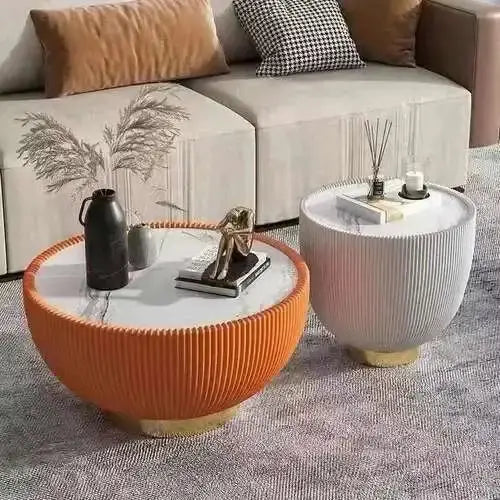 Two round coffee tables, one orange and one white, in a living room setting with a sofa and decorative items.