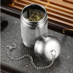 Stainless steel tea infuser with a chain, filled with loose tea leaves. Perfect for steeping fresh and flavorful tea effortlessly.