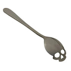 Stainless steel coffee spoon with skull-shaped cutout on white background
