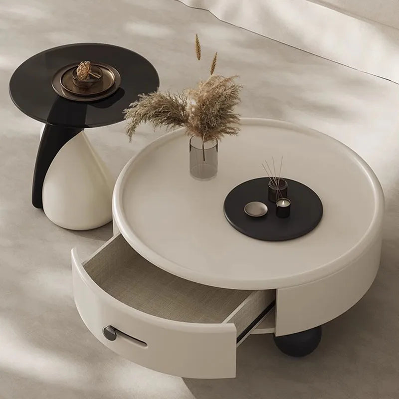Round coffee table with a drawer, black side table, and decorative items on a neutral background