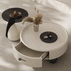 Round coffee table with a drawer, black side table, and decorative items on a neutral background