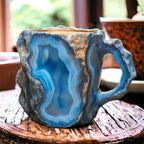 Colorful mineral crystal coffee mug in blue and grey with a jagged edge and ergonomic handle, set on a wooden surface.