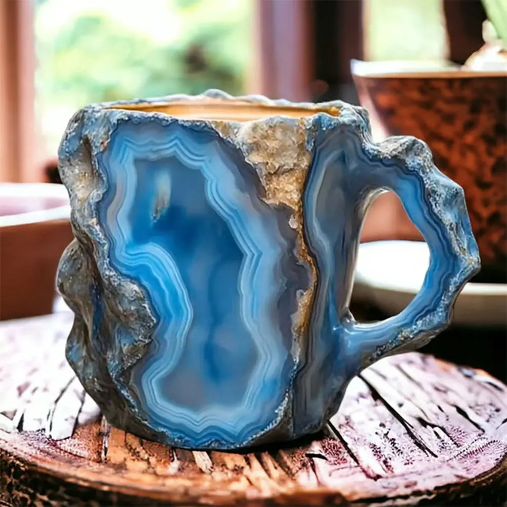 Colorful mineral crystal coffee mug in blue and grey with a jagged edge and ergonomic handle, set on a wooden surface.
