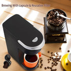 Electric travel coffee maker in black, brewing into a bright orange cup with coffee beans nearby.