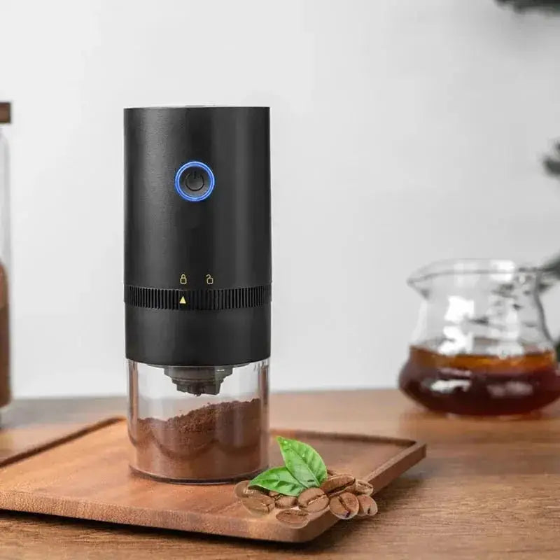 Portable USB coffee grinder with ceramic core, grinding fresh coffee beans on a wooden tray with coffee accessories in the background.