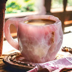 Pink marble-patterned mug with steaming coffee on a wooden coaster.