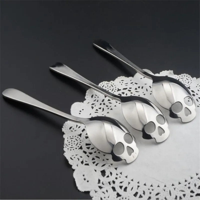 Three stainless steel skull spoons placed on a decorative lace doily. Perfect for coffee, tea, and desserts with a stylish gothic design.