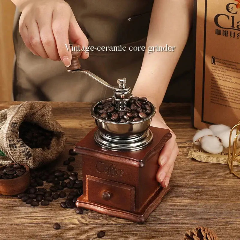 Person using a vintage ceramic core coffee grinder with coffee beans on a wooden table.