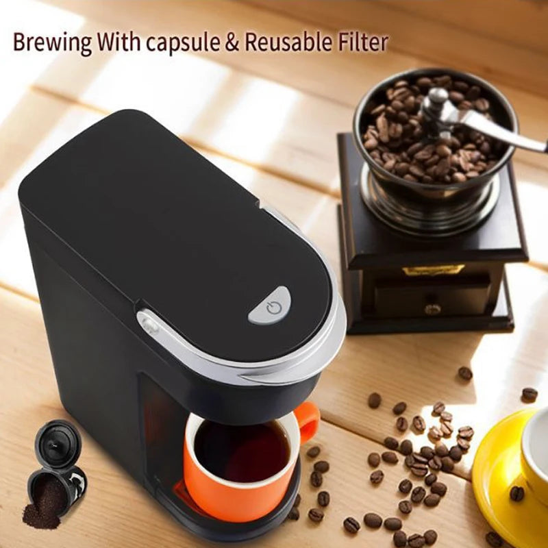 Black electric drip coffee maker with a silver trim, brewing into an orange cup, next to a coffee grinder and beans.