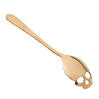 Gold coffee spoon with skull-shaped cutout design on a white background