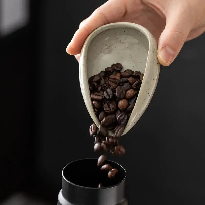 Ceramic coffee beans dosing cup with a tapered spout, pouring roasted coffee beans into a grinder. Ideal for precise espresso bean measurement.